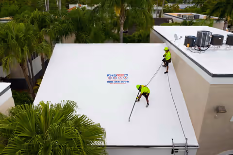 Aerial view of a flat white commercial roof with two crew members working and rope tie-downs