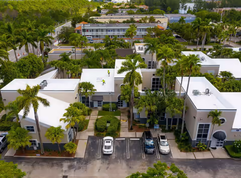 Aerial view of a low-rise townhouse complex with white wrapped roofs among palm trees