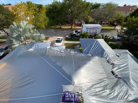 Aerial view of a roof covered with a silver-grey tarp tied down with rope